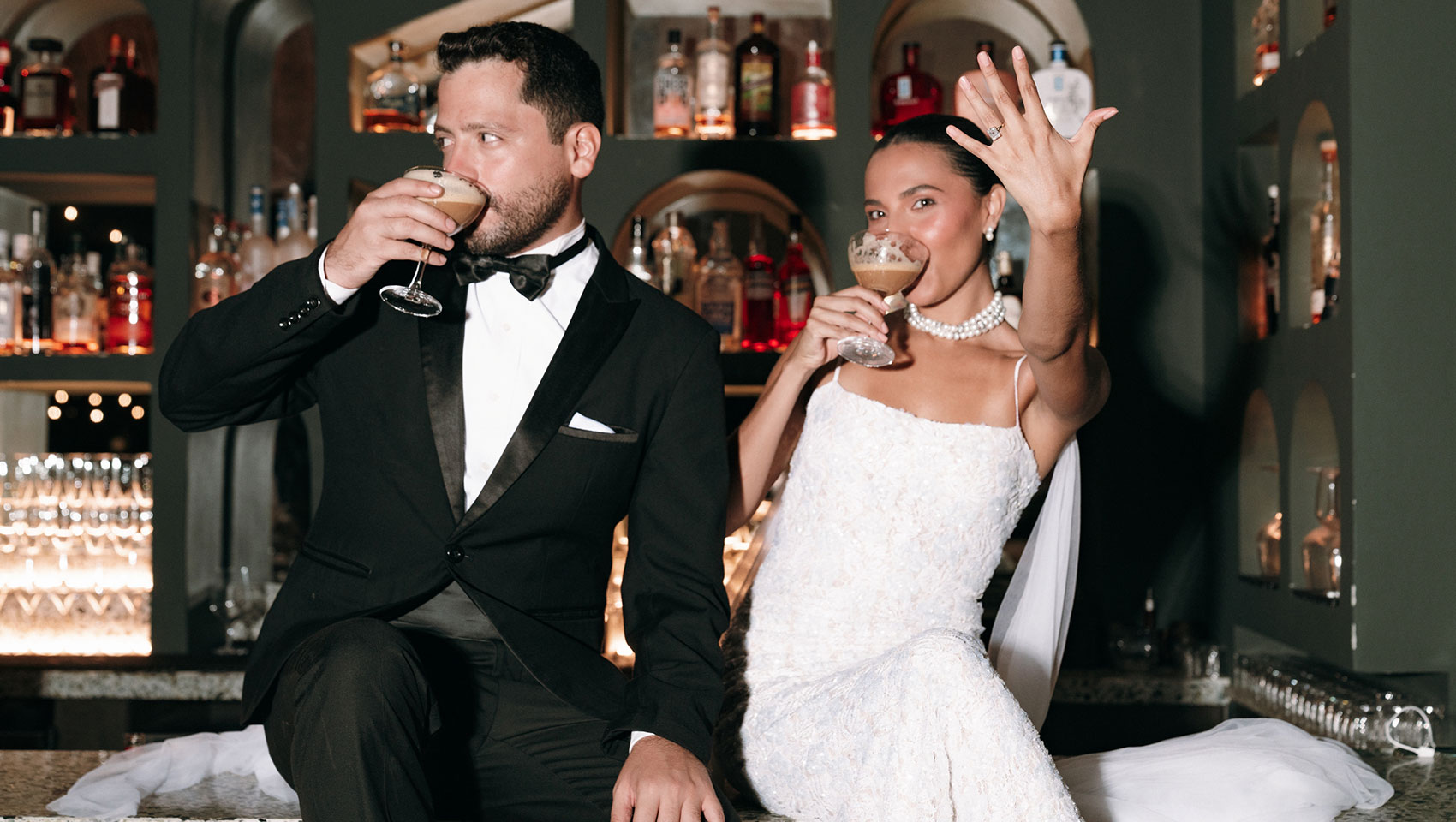 Bride sits next to groom on the bar each with a cocktail and she shows off her engagement ring at Kimpton Grand Roatan