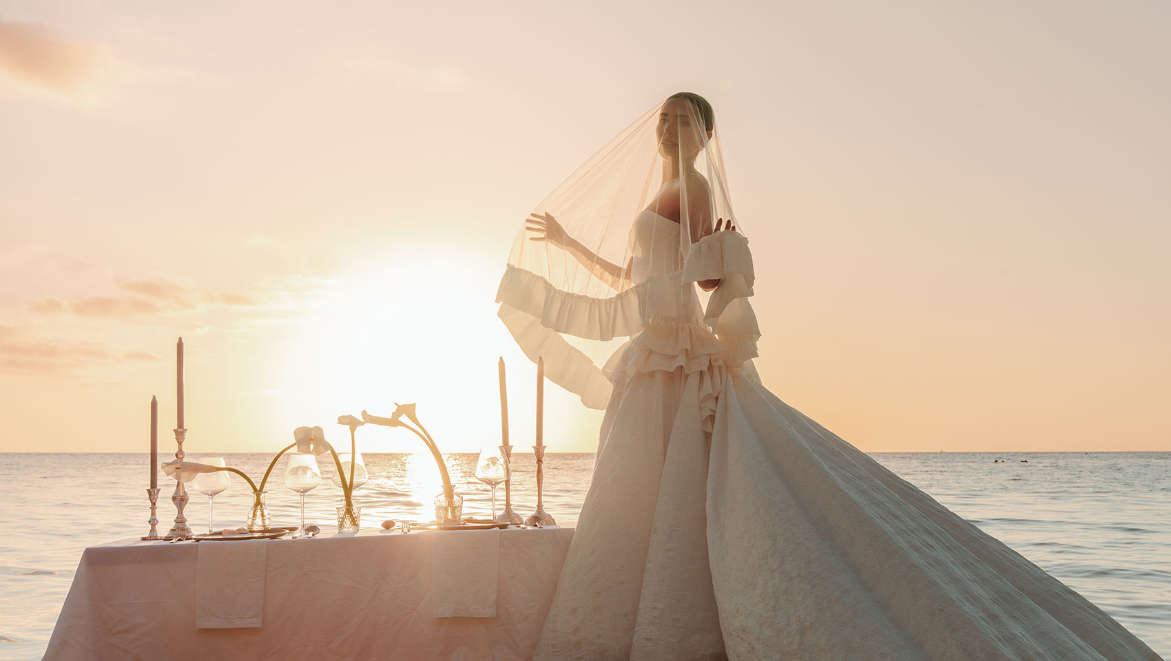 bride stands on a boat in the ocean at sunset at Kimpton Grand Roatan