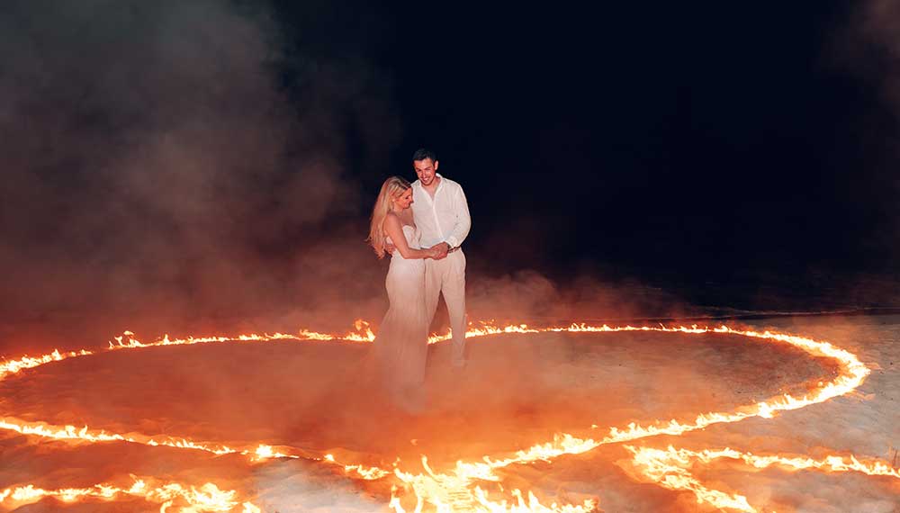 Bride and Groom on beach surrounded by a heart made of fire