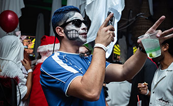 man with painted face and cocktail takes a photo of his drink at Kimpton Grand Roatan Halloween Party