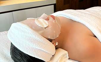woman receiving facial wears a mask and cucumbers on her eyes