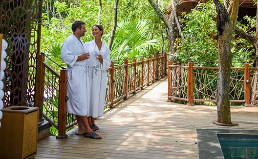 man and woman in robes stand beside Gran Roatan pool smiling with drinks