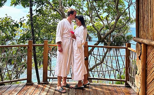 man and woman in robes stand on Grand Roatan terrace with drinks