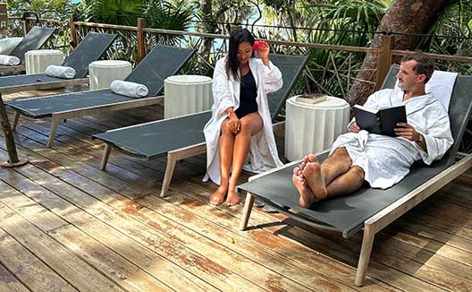Bcouple in robes relax poolside on lounge chairs